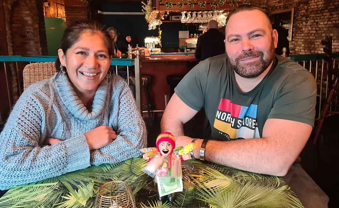 Valentina en Benny aan een tafel in de bar, met de Ekeko tussen hen in